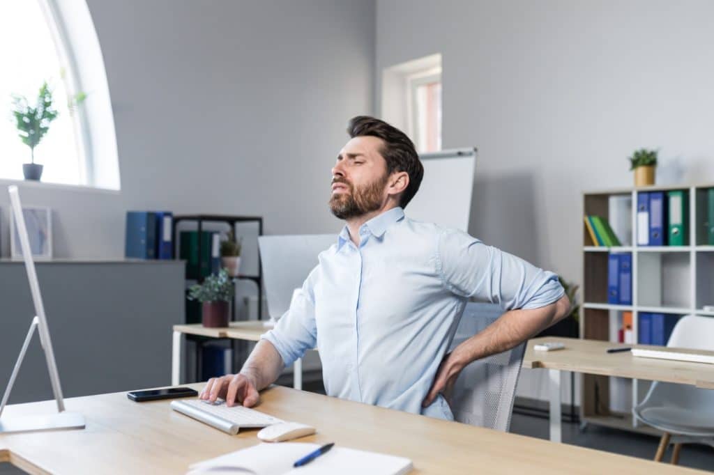A man suffers with back pain while at work at his desk