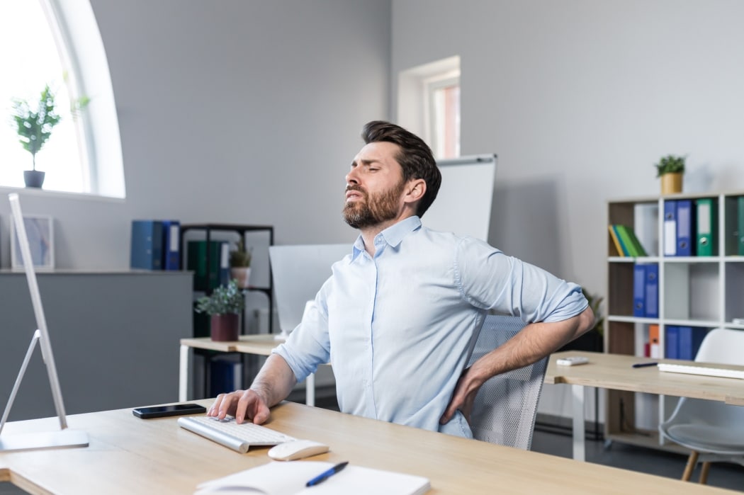A man suffers with back pain while at work at his desk