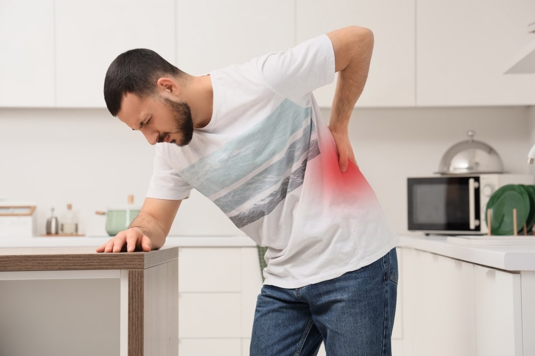A man suffers with back pain in his kitchen